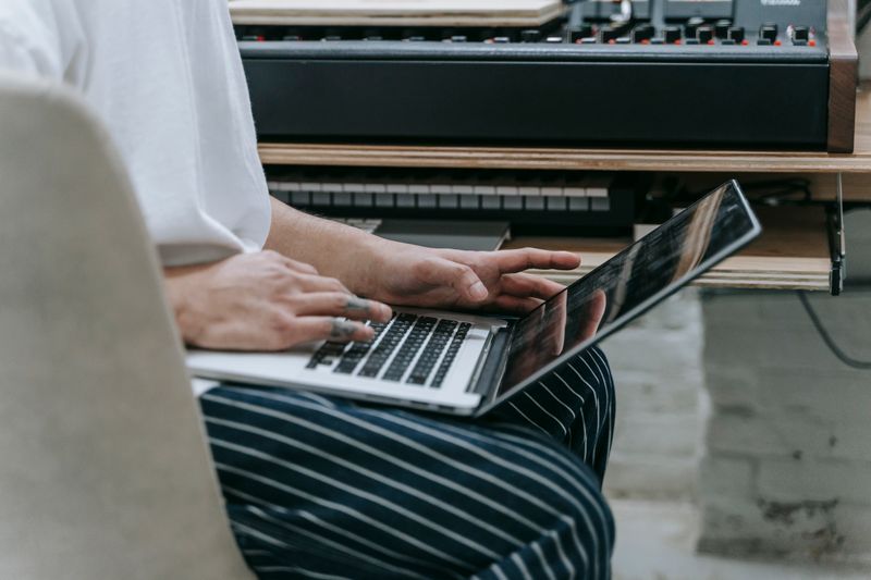 Person typing on laptop near a digital piano, highlighting a tech-savvy music workspace.