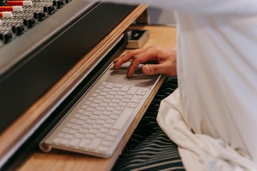 A person uses a wireless keyboard at a studio desk, illustrating modern music technology.