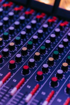 Vertical shot of a colorful audio mixer with various knobs in a studio setting.