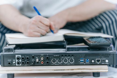 Free A detailed close-up of an audio mixer with a person taking notes in the background, highlighting focus and technology. Stock Photo
