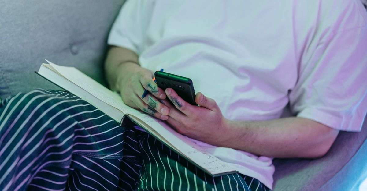 person sitting on a couch looking conflicted while holding a journal and a phone