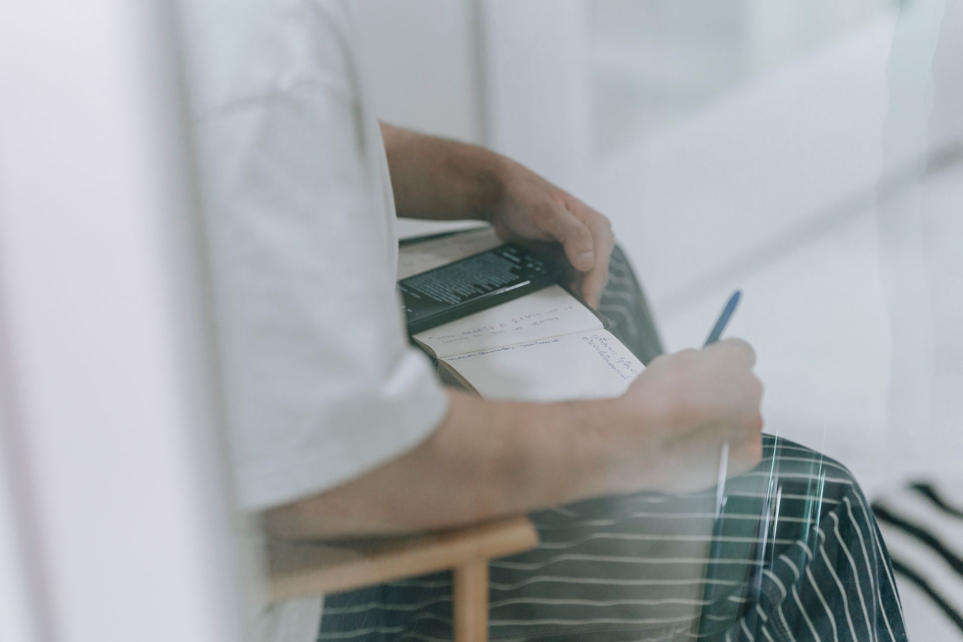 Casual scene of a person writing in a notebook, seen through glass.
