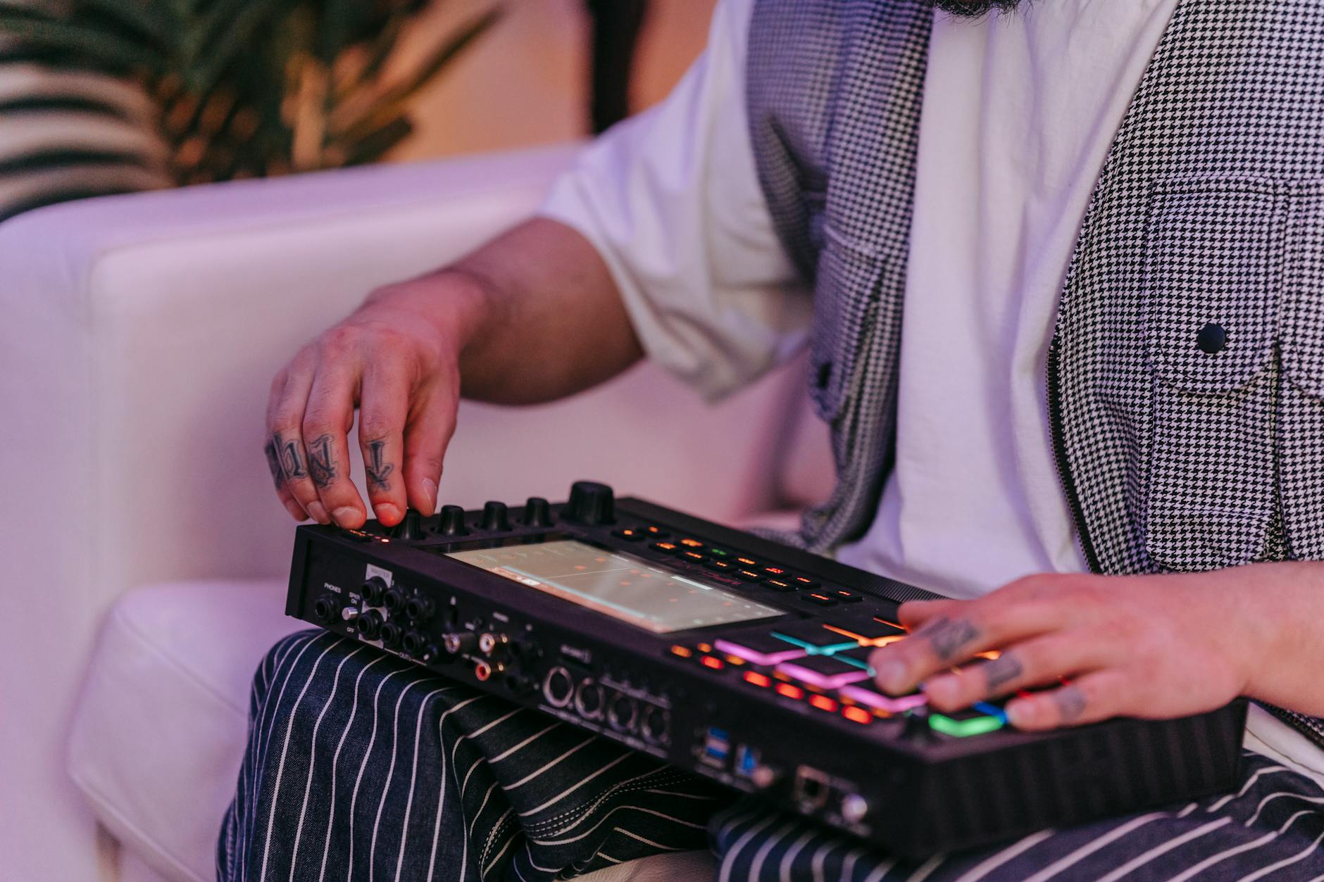 Close-up of a tattooed musician using an electronic audio mixer indoors. Modern