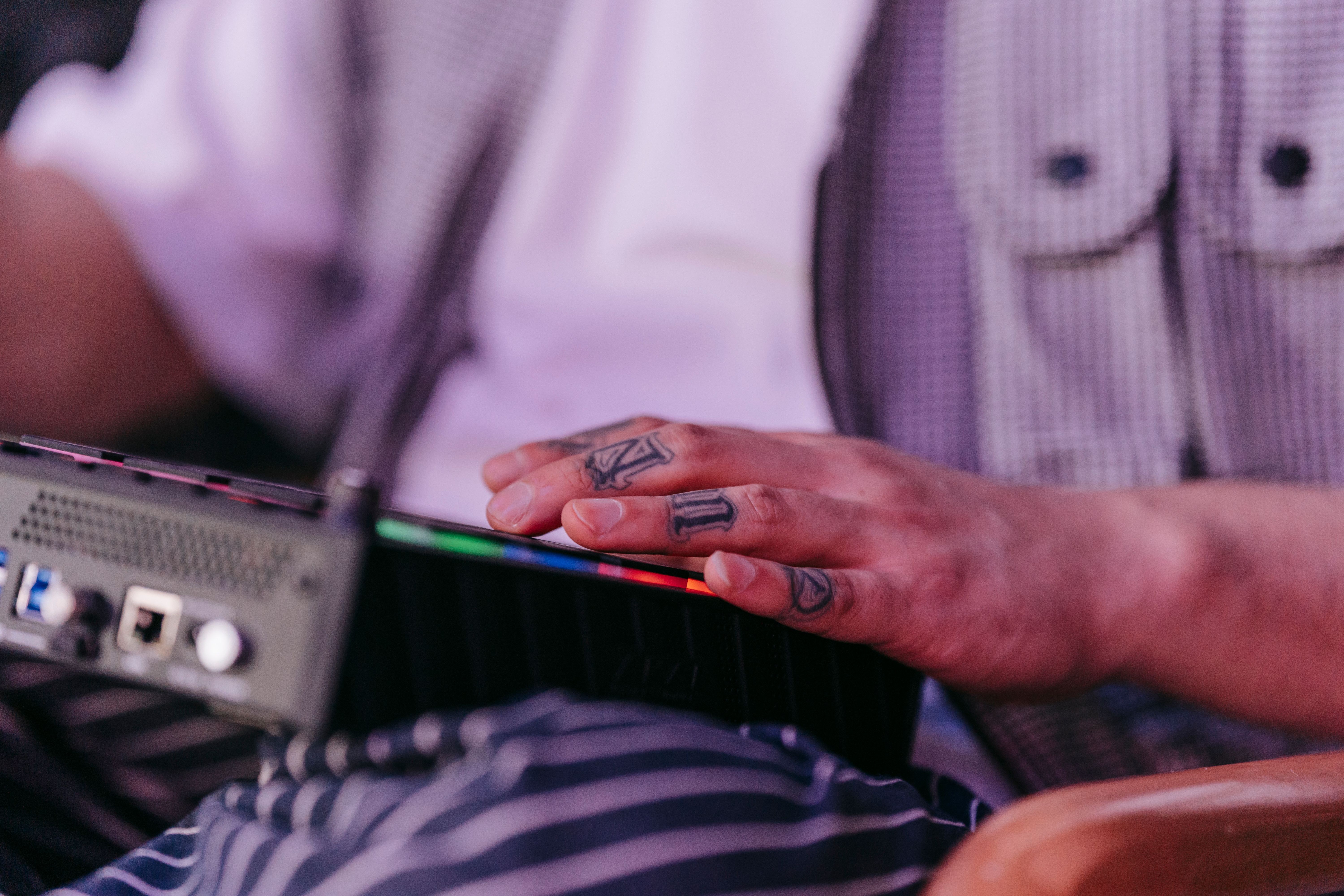 Tattooed hand adjusting controls on an audio mixer in a casual setting.