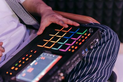 Hands playing a lit pad sampler on a lap in front of a foam wall