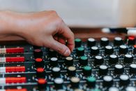 Close-up of a hand adjusting knobs on an audio mixer board in a studio setting.