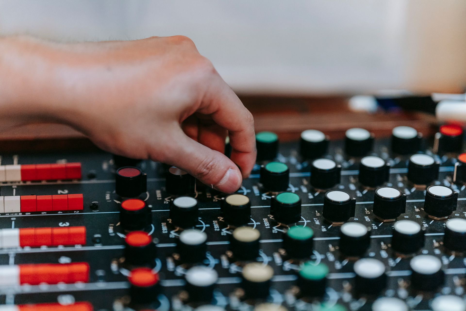 Close-up of a hand adjusting knobs on an audio mixer board in a studio setting.