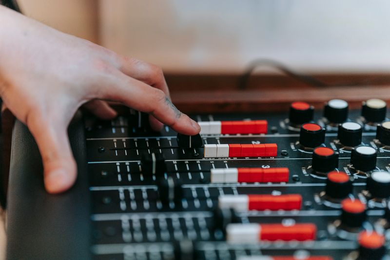 Mano deslizando los faders de una mesa de mezclas, con las teclas rojas y una luz cálida