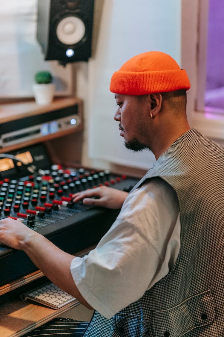 A Man Wearing Orange Beanie Using Audio Mixer