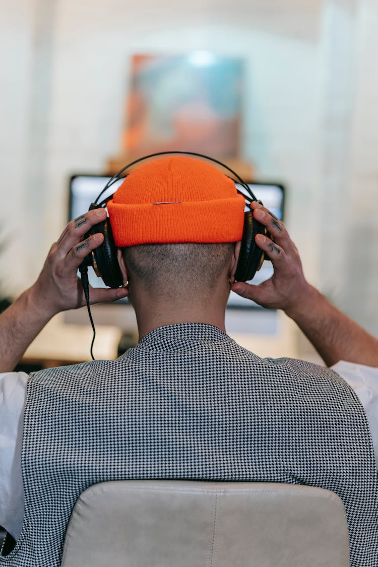 Person Wearing An Orange Beanie Listening To The Headphones