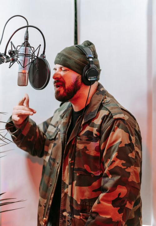 Free Musician in studio wearing headphones and camo jacket, mid-song expression. Stock Photo