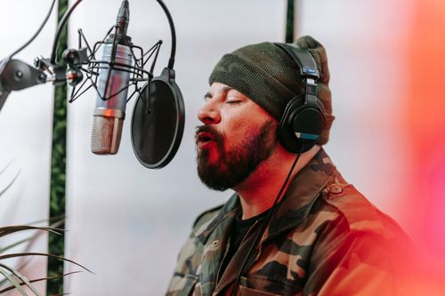 Free Bearded man in camouflage jacket singing into a microphone in a studio setting. Stock Photo