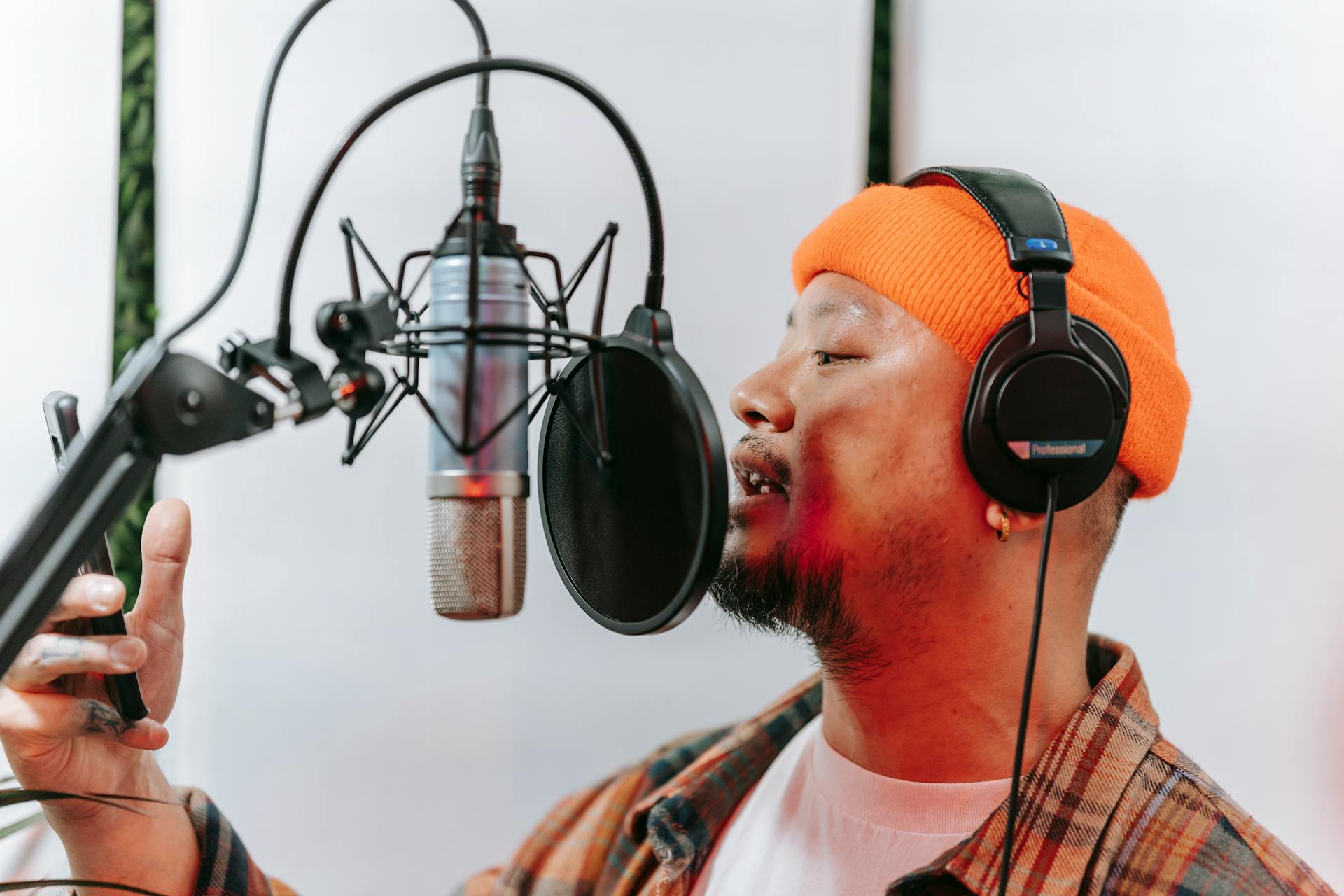 Male singer with headphones recording vocals using a condenser microphone in a music studio.