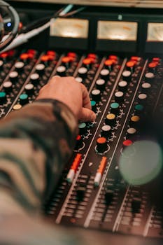Close-up of a hand adjusting controls on an audio mixer in a music studio, showcasing detailed electronic equipment.