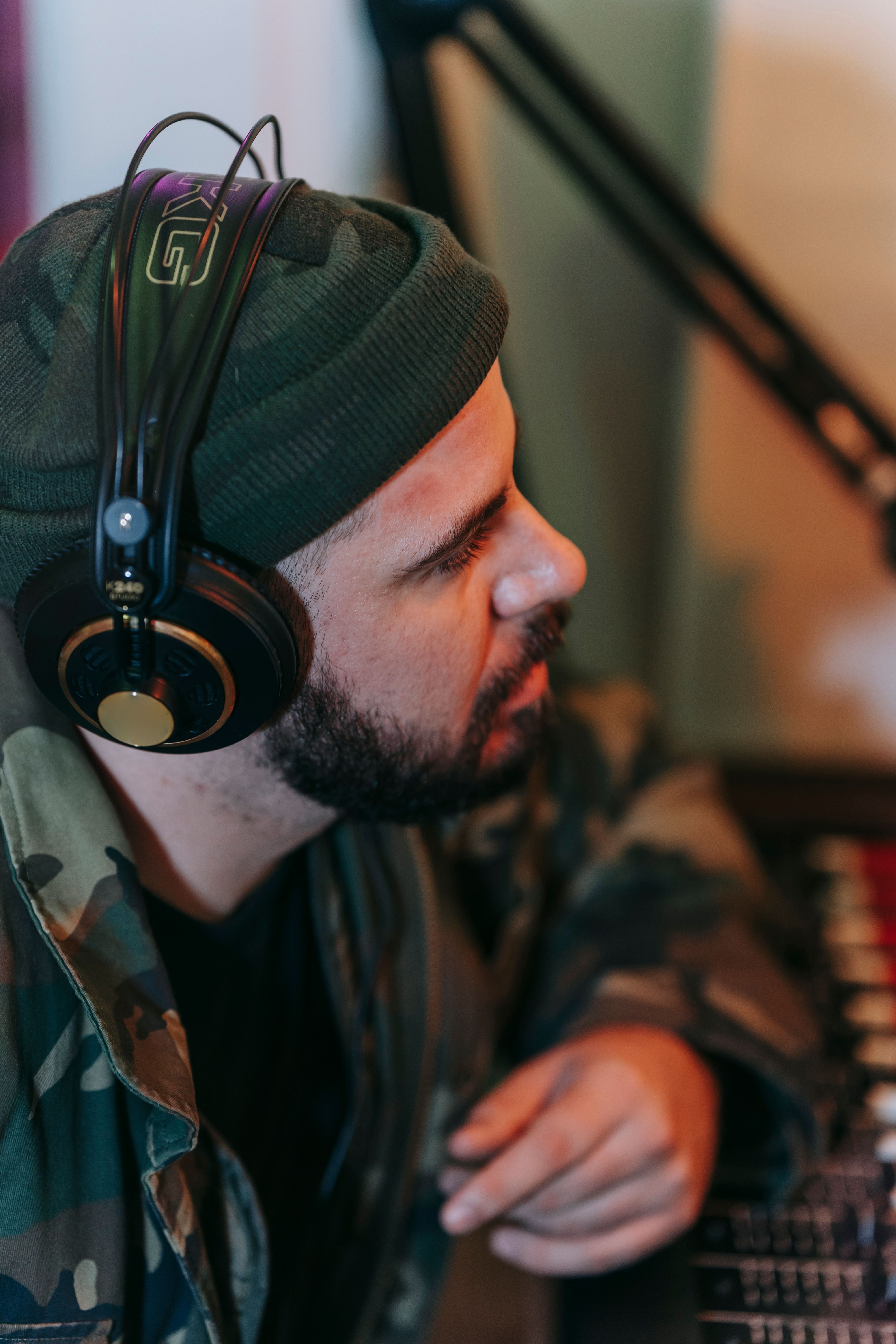 A bearded music producer deep in thought wearing headphones in a studio.