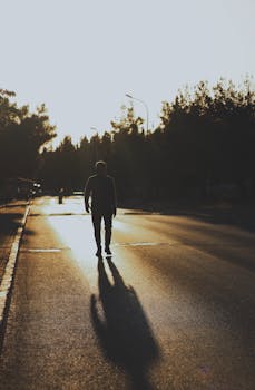 A solitary figure walks on a deserted road at sunset, casting a long shadow.