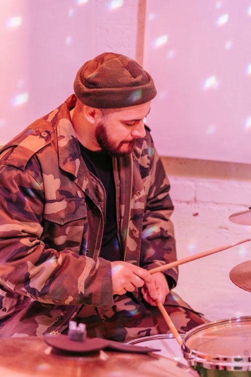 Free A drummer in camouflage attire plays a drum kit indoors, focusing intently. Stock Photo