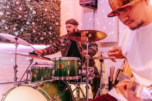 Free Musicians playing drums and guitar in a modern studio with a leafy backdrop. Stock Photo