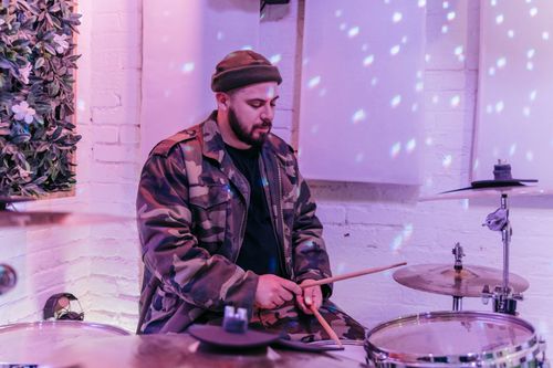 Free A man wearing a beanie and camouflage jacket playing drums in a cozy studio setting. Stock Photo