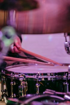 Close-up shot of a drummer playing a drum kit with vibrant lighting and focus on the hands.