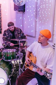 Musicians playing guitar and drums in a studio setting with a disco ball and starry lights.
