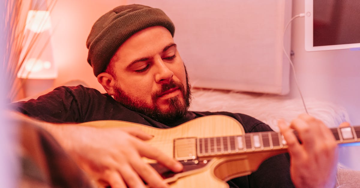 Man in beanie hat playing electric guitar, creating music in a cozy home studio.