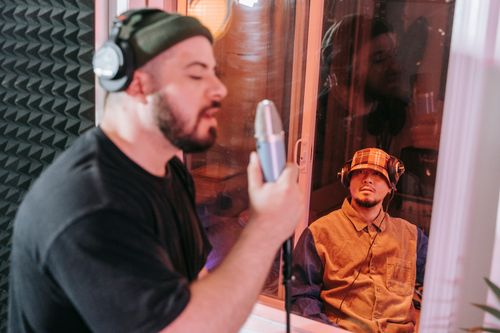 Free Singer recording a track in a studio with producer observing through glass. Captured in a creative music environment. Stock Photo