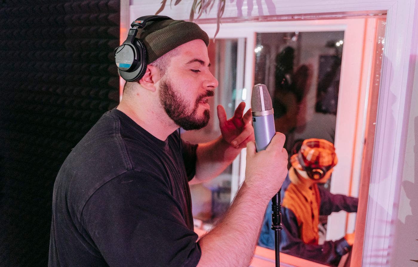 Vokalis memakai headphone dan bernyanyi di depan mikrofon dalam sesi rekaman studio