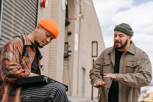 Free Two adults in plaid shirts and beanies having a casual conversation on the street. Stock Photo