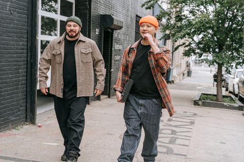 Free Two men in beanies and plaid shirts walking on a city sidewalk, showcasing urban fashion. Stock Photo