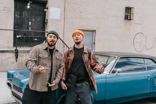 Free Two men in stylish attire leaning against a vintage blue car on a city street. Stock Photo