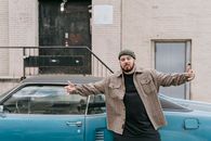 Man in Gray and White Plaid Coat Leaning on Blue Car
