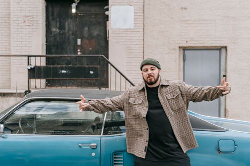 Free Man in plaid jacket and beanie standing by vintage blue car on urban street. Stock Photo