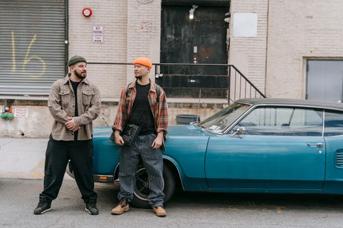 Free Two men in casual urban outfits stand beside a vintage blue car on a city street. Stock Photo