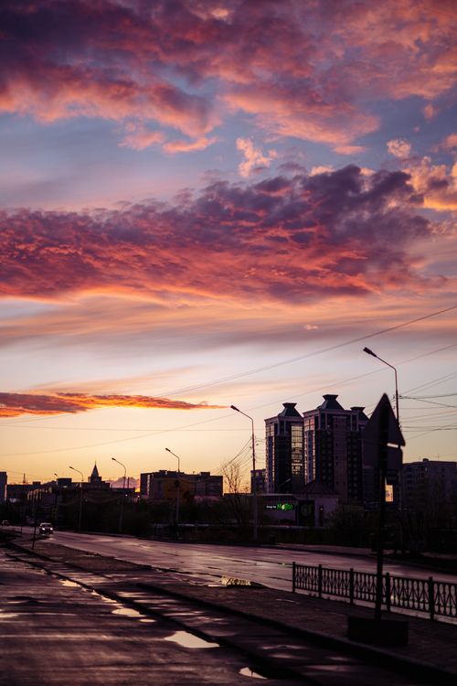 Free A vibrant sunset creating dramatic silhouettes of city buildings and clouds. Stock Photo