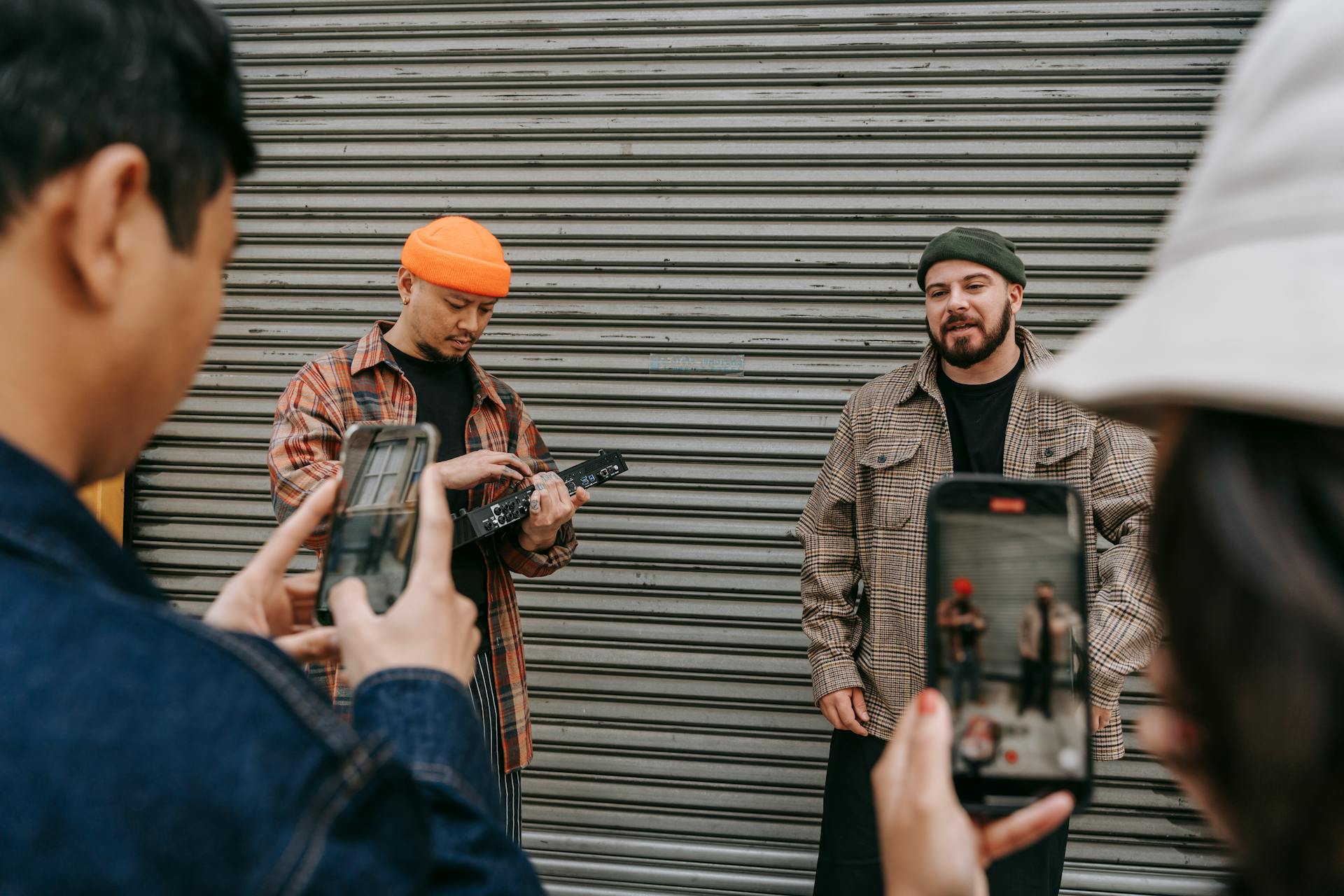 Street performers playing music while being filmed by a small crowd with smartphones.