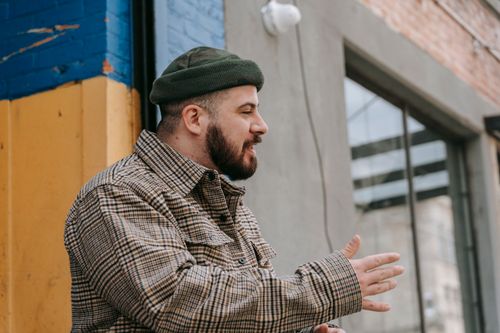 Free A bearded man in a plaid shirt and knitted cap in an urban environment, side view. Stock Photo