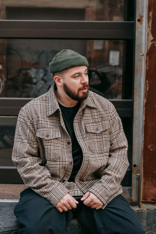 Free Casual urban scene with bearded man in plaid jacket and beanie sitting outdoors. Stock Photo