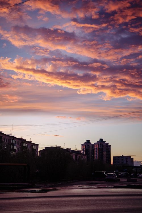 Free Silhouette of urban buildings against a vibrant sky at sunset, featuring dramatic clouds. Stock Photo