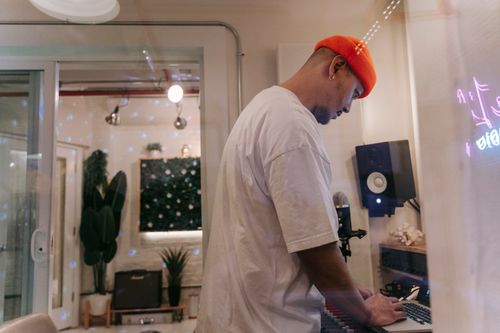 Free Asian man in a beanie working on music production in a modern studio with laptop and keyboard. Stock Photo