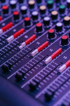 A detailed view of a sound mixer panel with red knobs and sliders, showing selective focus.