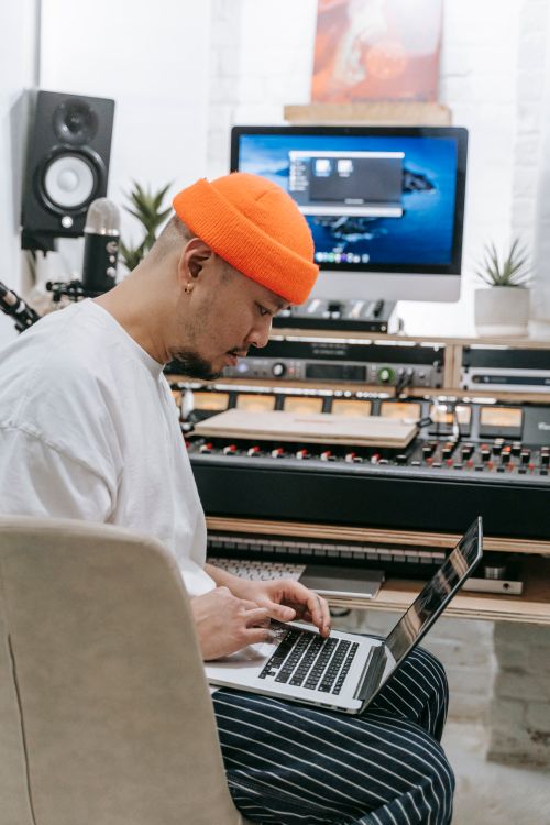 Free Asian man wearing orange beanie using laptop in modern home music studio. Stock Photo