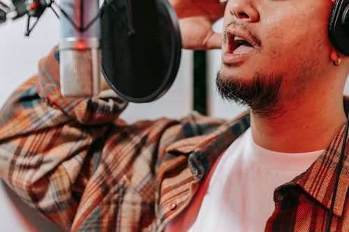 Man in White Crew Neck Shirt Wearing Brown Plaid Button Up Shirt Near a Microphone