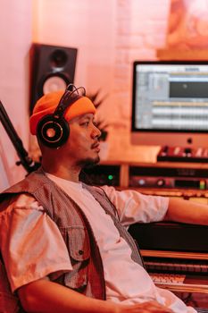 A man wearing headphones and a beanie focused on producing music in a modern studio.