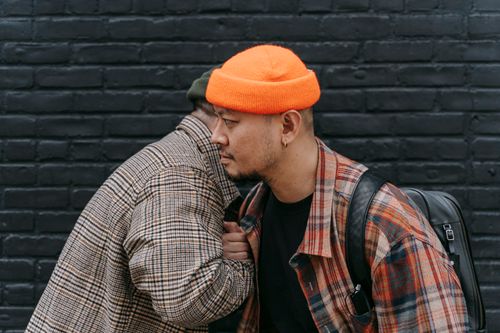 Free Two men wearing plaid jackets and beanies stand against a brick wall, portraying urban style. Stock Photo