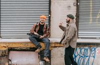 Man in Brown and White Plaid Dress Shirt and Orange Knit Cap Sitting on Brown Wooden
