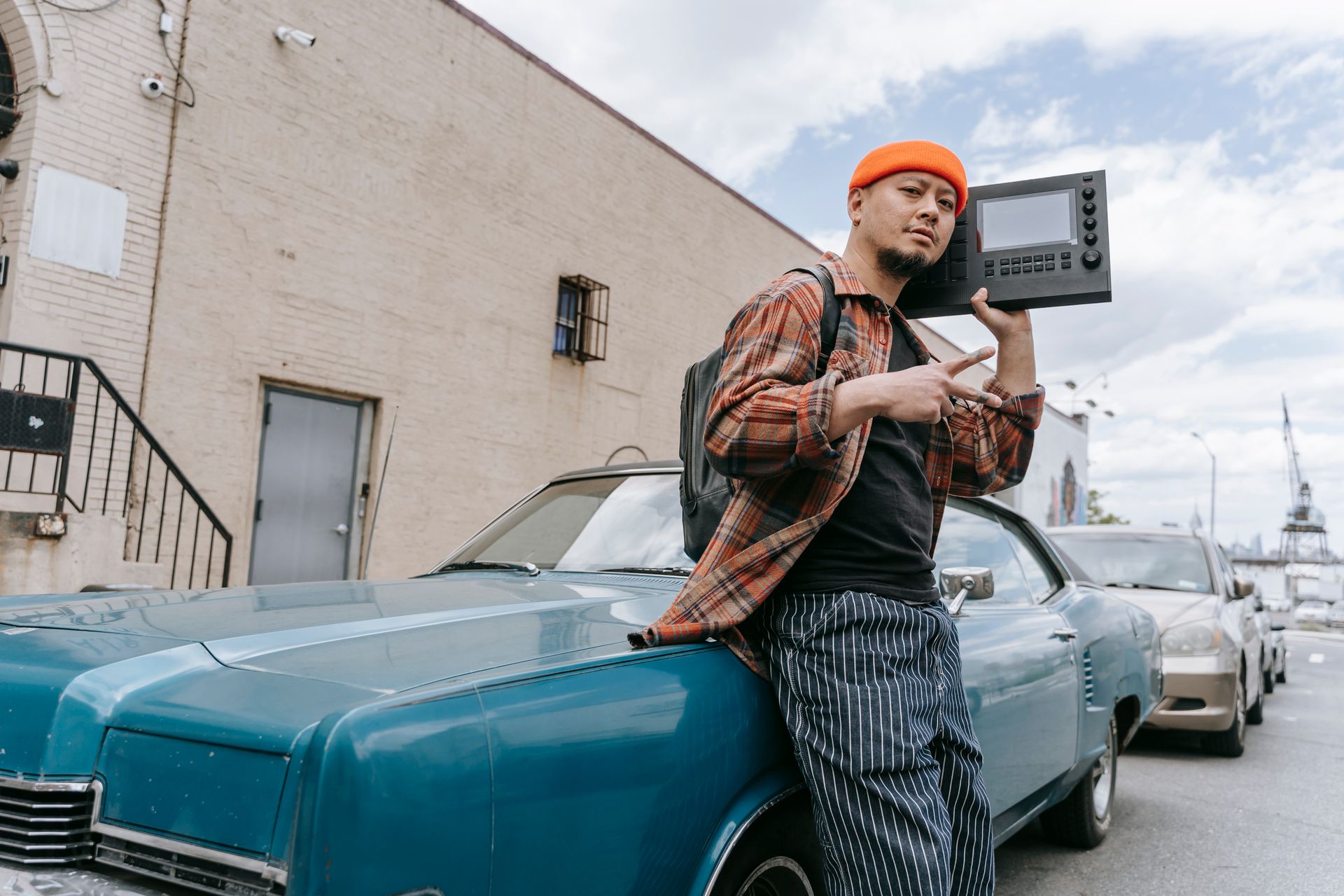 Hip urban man posing with a retro car, holding a music device, showing peace sign.