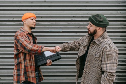 Free Two men wearing beanies exchanging a fist bump in front of an urban background. Stock Photo
