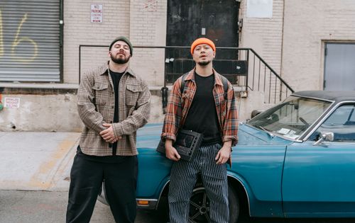 Free Two stylish men pose confidently by a vintage blue car in an urban setting. Stock Photo