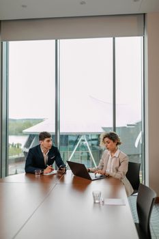 Two professionals engaged in a business meeting with laptops in a modern office setting.